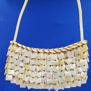 May include: A white and brown handbag made of small, square, iridescent shell pieces. The bag has a single strap.