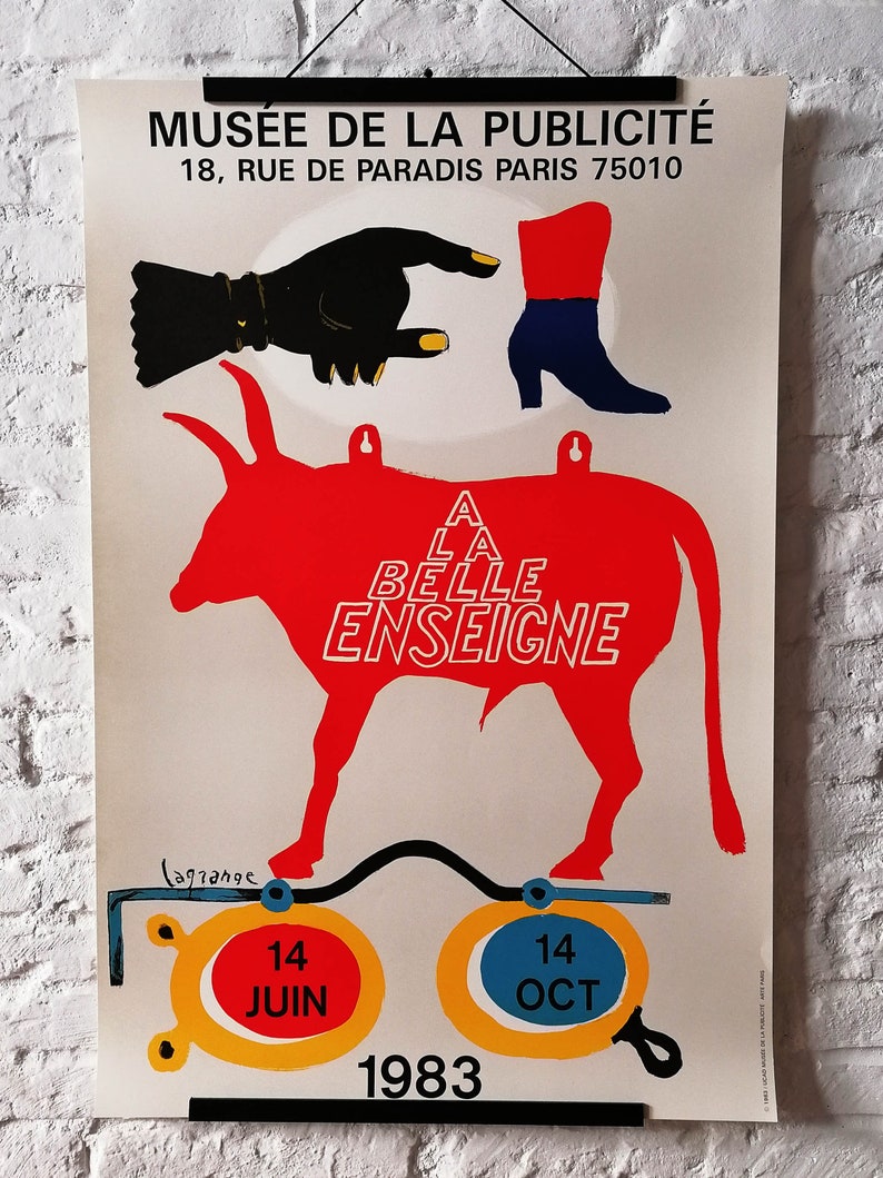K&ouml;nnte beinhalten: Vintage-Poster f&uuml;r das Mus&eacute;e de la Publicit&eacute; mit einer roten Bullensilhouette und dem Text "A LA BELLE ENSEIGNE". Das Poster zeigt eine schwarze Hand, einen roten und blauen Stiefel sowie die Daten: 14. Juni und 14. Oktober 1983.