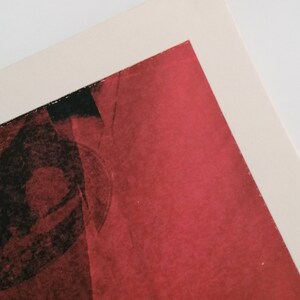 Puede incluir: Un primer plano de una pintura abstracta roja y negra. La pintura tiene una superficie texturizada y parece estar hecha con un pincel.