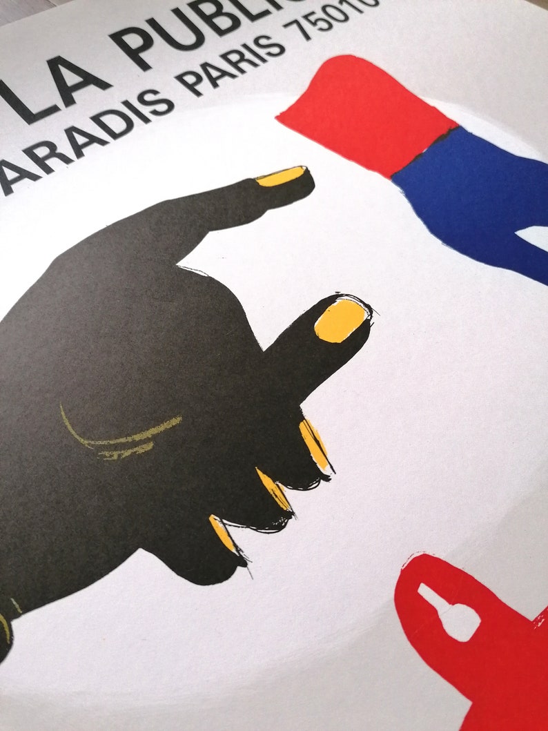 K&ouml;nnte beinhalten: Grafikdruck mit einer schwarzen Hand mit gelben Fingern&auml;geln, die nach einer roten und blauen Hand greift. Der Druck tr&auml;gt den Text "LA PUBLI PARADIS PARIS 75010" oben.