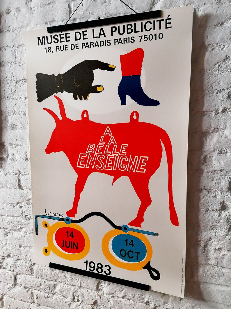K&ouml;nnte beinhalten: Plakat f&uuml;r das Mus&eacute;e de la Publicit&eacute; mit einer roten Stier-Silhouette und dem Text "A LA BELLE ENSEIGNE". Das Plakat zeigt eine schwarze Hand, einen roten und blauen Stiefel und die Daten: 14. Juni und 14. Oktober 1983.