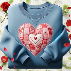 May include: A pale blue sweatshirt with a large patchwork heart motif. The heart is made from various pink and red patterned fabrics, with a smaller heart at the centre. Red rose petals and white flowers surround the sweatshirt.
