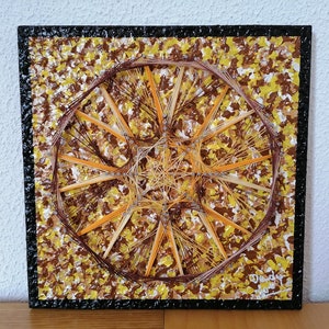 May include: Square artwork featuring a geometric design created with brown and orange string on a textured background of yellow, brown, and white paint. The artwork has a black border and is signed in the bottom right corner.