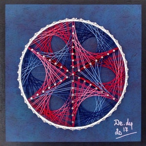 May include: A circular string art piece with a geometric design in red, white, and blue. The artwork is set against a dark blue background within a black frame. The piece features a star-like pattern created by the interwoven strings.