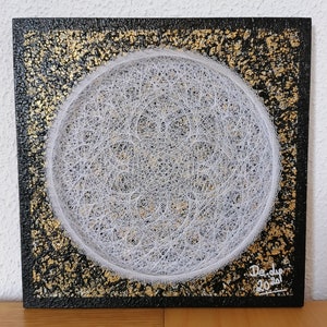May include: Square artwork with a black background and gold accents. A white string art circle is centered on the square. The artwork is signed "Derdip 2021".