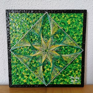 May include: A square string art piece with a green and yellow geometric design. The artwork features a diamond shape with a starburst pattern in the center, set against a textured green background and a black border.