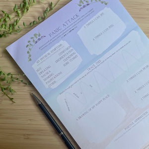 May include: A printable worksheet with a light blue background and lavender floral accents. The worksheet is titled "Panic Attack" and includes a list of physical symptoms, a section to trace a breathing pattern, a space to draw a happy place, and a section for positive affirmations.