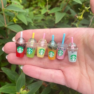 May include: Six miniature plastic cups with straws and black boba balls, filled with different coloured liquids. The cups are arranged in a row on a hand, with the red cup on the left and the blue cup on the right.