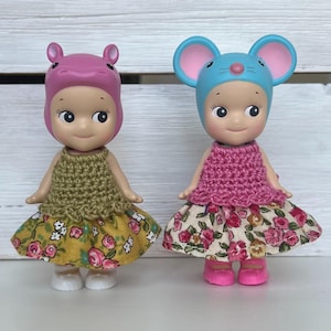 Puede incluir: Dos peque&ntilde;as figuras, una con un sombrero de hipop&oacute;tamo rosa y otra con un sombrero de rat&oacute;n azul. Ambas visten tops de ganchillo y faldas con estampado floral. La figura del hipop&oacute;tamo tiene una falda amarilla, y la figura del rat&oacute;n tiene una falda floral.