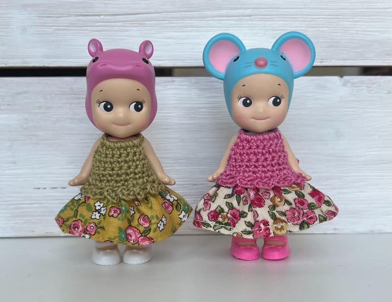Puede incluir: Dos peque&ntilde;as figuras, una con un sombrero de hipop&oacute;tamo rosa y otra con un sombrero de rat&oacute;n azul. Ambas visten tops de ganchillo y faldas con estampado floral. La figura del hipop&oacute;tamo tiene una falda amarilla, y la figura del rat&oacute;n tiene una falda floral.