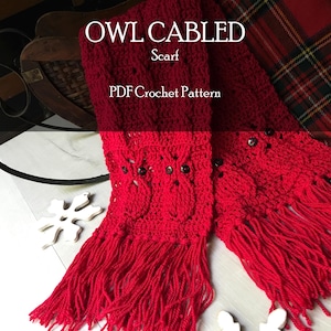 Könnte beinhalten: Ein roter, gefranster, gehäkelter Schal mit einem Eulenmuster. Der Schal trägt den Text "OWL CABLED Scarf PDF Crochet Pattern". Das Eulenmuster ist auf dem Schal sichtbar, mit dunklen Knöpfen als Augen. Der Schal ist aus einem weichen, strukturierten Garn gefertigt.