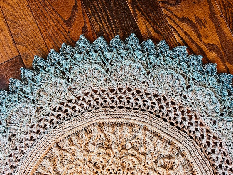 Pu&ograve; includere: Un centrino all'uncinetto circolare con un intricato motivo a mandala. Il centro &egrave; beige chiaro, che sfuma in un delicato gradiente di blu-verde tenue sul bordo esterno smerlato. Il design presenta punti densi e lavorazione a pizzo.
