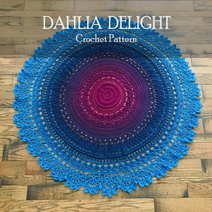 Può includere: Un centrino circolare all'uncinetto caratterizzato da un vivace gradiente di colore che passa da un centro magenta intenso a sfumature di viola, blu navy e blu brillante sul bordo esterno. Il testo DAHLIA DELIGHT Crochet Pattern è stampato sopra.