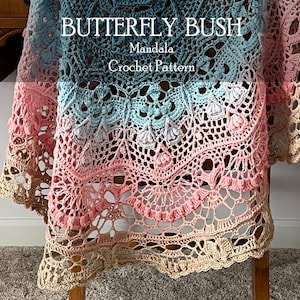 May include: A crochet mandala with a gradient color scheme transitioning from teal to pink and beige. The textile features intricate openwork, floral motifs, and textured stitches. The text "BUTTERFLY BUSH Mandala Crochet Pattern" is printed on the image.