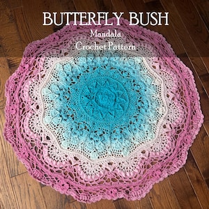 Op de afbeelding: Een cirkelvormig gehaakt mandala met een kleurverloop dat overgaat van een diep turquoise centrum naar lichtblauw, lichtroze en uiteindelijk een donker magenta buitenrand. De tekst BUTTERFLY BUSH Mandala Crochet Pattern is zichtbaar.