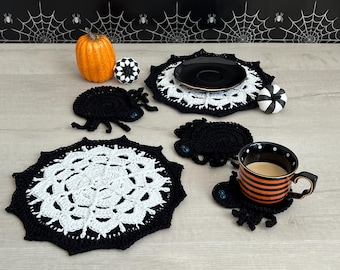 May include: Two round crochet doilies featuring a white spiderweb pattern on a black background, accompanied by three black crochet spider coasters with blue button eyes, a small orange pumpkin, and two black and white striped pumpkins.