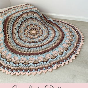 May include: Crochet pattern for a Marigold Magic Mandala. The mandala is a large, circular design with multiple colors, including brown, beige, blue, and pink. The pattern is available for purchase on Etsy.