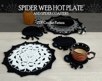 May include: A PDF crochet pattern titled SPIDER WEB HOT PLATE AND SPIDER COASTERS featuring black and white crocheted spider web hot plates and black spider-shaped coasters with blue button eyes, displayed with a striped mug and small pumpkins.