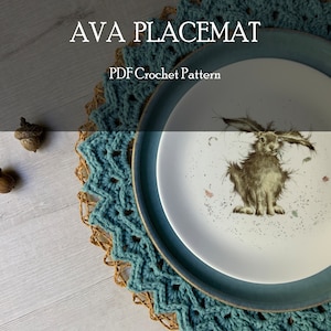 Può includere: Un sottopiatto in crochet turchese con una base intrecciata marrone, su cui è posto un piatto bianco con un'illustrazione di un coniglio marrone. Il testo "AVA PLACEMAT PDF Crochet Pattern" è visualizzato sopra il sottopiatto.