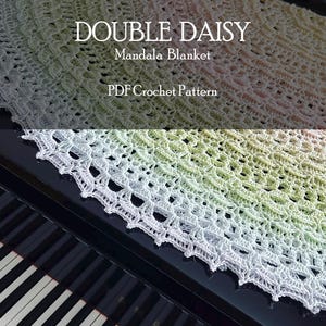May include: A round, crocheted mandala blanket featuring a gradient of white, light green, and soft pink hues. The text "DOUBLE DAISY Mandala Blanket PDF Crochet Pattern" is overlaid on the image. The blanket rests on a black piano keyboard.