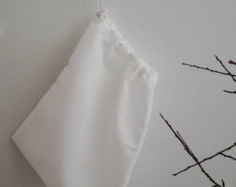 May include: A white drawstring bag hanging from a white hook on a white wall.