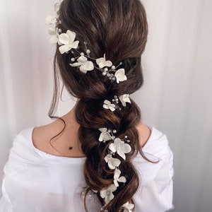 Könnte beinhalten: Ein weißer Blumenhaarschmuck mit Perlenakzenten. Der Haarschmuck besteht aus zarten weißen Blüten und Perlen und ist perfekt für eine Hochzeit oder einen anderen besonderen Anlass.