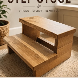 Op de afbeelding: Een houten opstapje met twee treden en een natuurlijke lichtbruine houtnerfafwerking. De tekst luidt: HANDMADE STEP STOOL, STRONG STURDY BEAUTIFUL, SOLID WOOD BUILT TO LAST, SAFE STABLE FOR EVERYDAY USE, PERFECT FOR HOME KIDS, MADE WITH CARE HANDMADE QUALITY, ELEVATE EVERYDAY MOMENTS.