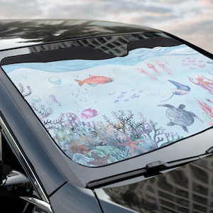 May include: A colourful car sunshade featuring an underwater scene with fish, coral, and a sea turtle. The sunshade is designed to block sunlight and heat from entering the car.