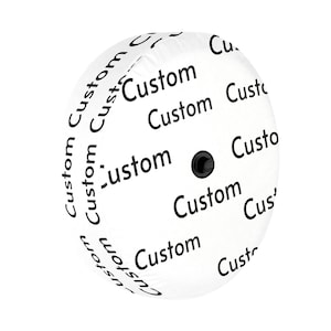 May include: A circular white spare tire cover featuring a repeating pattern of the word Custom printed in black text. The cover has a smooth, rounded surface with a small black circular attachment point located in the center of the design.