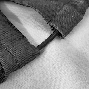 May include: A dark gray, textured fabric strap assembly featuring two parallel sections connected by a thin, black elastic cord. The fabric has a visible woven grid pattern and reinforced stitching along the edges, creating a durable, functional component.