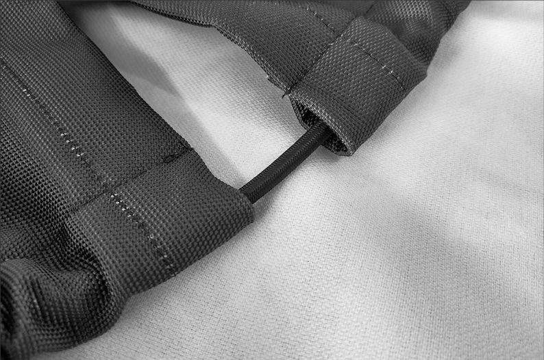 May include: A dark gray, textured fabric strap assembly featuring two parallel sections connected by a thin, black elastic cord. The fabric has a visible woven grid pattern and reinforced stitching along the edges, creating a durable, functional component.