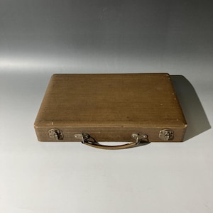 Puede incluir: Un malet&iacute;n rectangular de color marr&oacute;n con una superficie texturizada y acanalada. El estuche cuenta con un asa curva unida al panel frontal y dos cierres met&aacute;licos en el borde inferior. El exterior tiene un acabado marr&oacute;n uniforme.