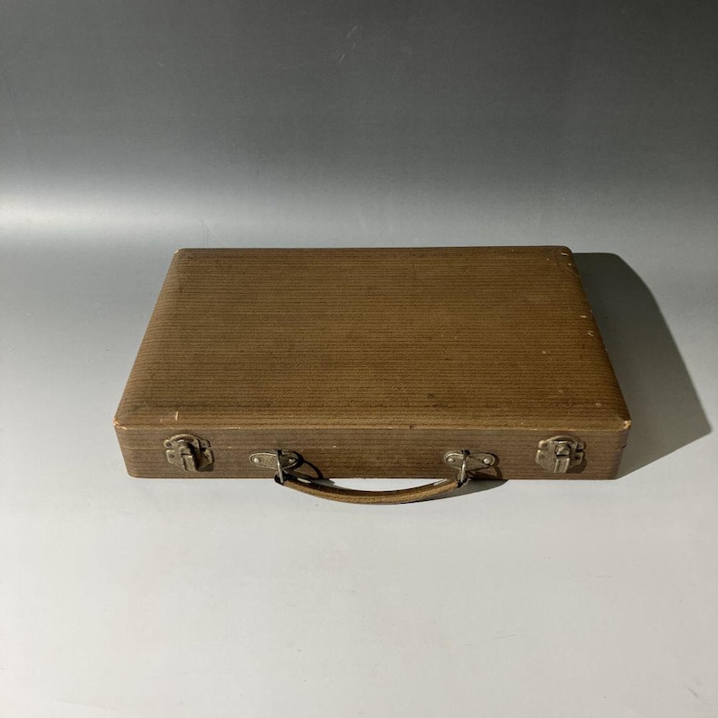 Puede incluir: Un malet&iacute;n rectangular de color marr&oacute;n con una superficie texturizada y acanalada. El estuche cuenta con un asa curva unida al panel frontal y dos cierres met&aacute;licos en el borde inferior. El exterior tiene un acabado marr&oacute;n uniforme.