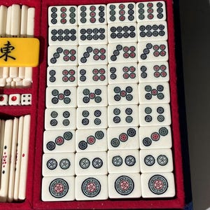 May include: A vintage Mahjong set in a blue velvet case with red lining. The ivory-colored tiles feature black, red, and green symbols and numbers. Includes dice and a yellow tile with a black character.