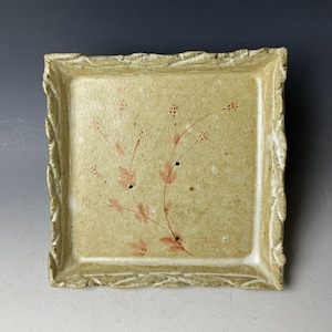 以下が含まれることがあります： 薄い茶色の釉薬と装飾的な縁取りが施された正方形の陶器のトレイ。トレイには、赤と緑の植物の枝が手描きで描かれています。