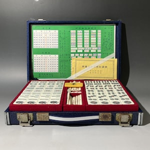 May include: Open blue velvet-lined mahjong set with ivory tiles, a red felt base, and a green chart. The set includes a variety of tiles, dice, and a small yellow tile holder. The case is closed with metal clasps.