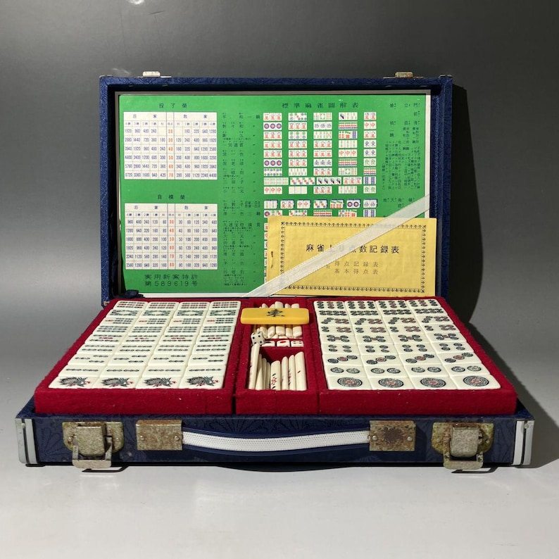 May include: Open blue velvet-lined mahjong set with ivory tiles, a red felt base, and a green chart. The set includes a variety of tiles, dice, and a small yellow tile holder. The case is closed with metal clasps.