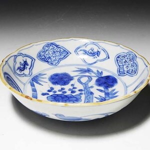 Könnte beinhalten: Eine weiße Porzellanschale mit blau-weißem Design. Die Schale hat einen gewellten Rand und zeigt ein zentrales Design eines Baumes mit Bambus und Vögeln. Die Schale ist mit anderen Motiven verziert, darunter geometrische Muster und chinesische Schriftzeichen.
