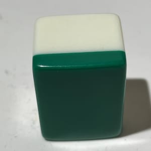 Pu&ograve; includere: Una tessera rettangolare da mahjong caratterizzata da una sezione superiore bianca liscia e una sezione inferiore verde pi&ugrave; ampia. La tessera presenta angoli arrotondati e una finitura lucida, offrendo un aspetto bicolore senza segni o incisioni.