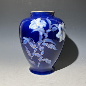 Puede incluir: Un jarrón de cerámica azul cobalto con borde dorado y diseño floral. El jarrón presenta flores blancas y azul claro con detalles dorados. Las flores y hojas están pintadas sobre la superficie del jarrón, creando una pieza decorativa.