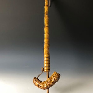 May include: A long, carved bamboo smoking pipe with a curved bowl. The pipe is decorated with intricate patterns and has a string attached to the bowl.