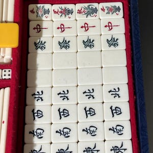 May include: A vintage Mahjong set with ivory-colored tiles, each displaying Chinese characters and decorative floral designs. The set is housed in a blue case with a red velvet interior, including dice and ivory-colored sticks.