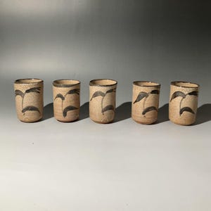 May include: Five ceramic tumblers with a beige crackle glaze and dark brown leaf designs. The rims are also dark brown. These decorative cups are ideal for serving beverages.