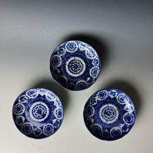 Könnte beinhalten: Drei kleine blaue und weiße Keramikteller mit aufwendigen Blumendesigns. Die Teller haben einen erhöhten Rand und einen leicht gewellten Rand.