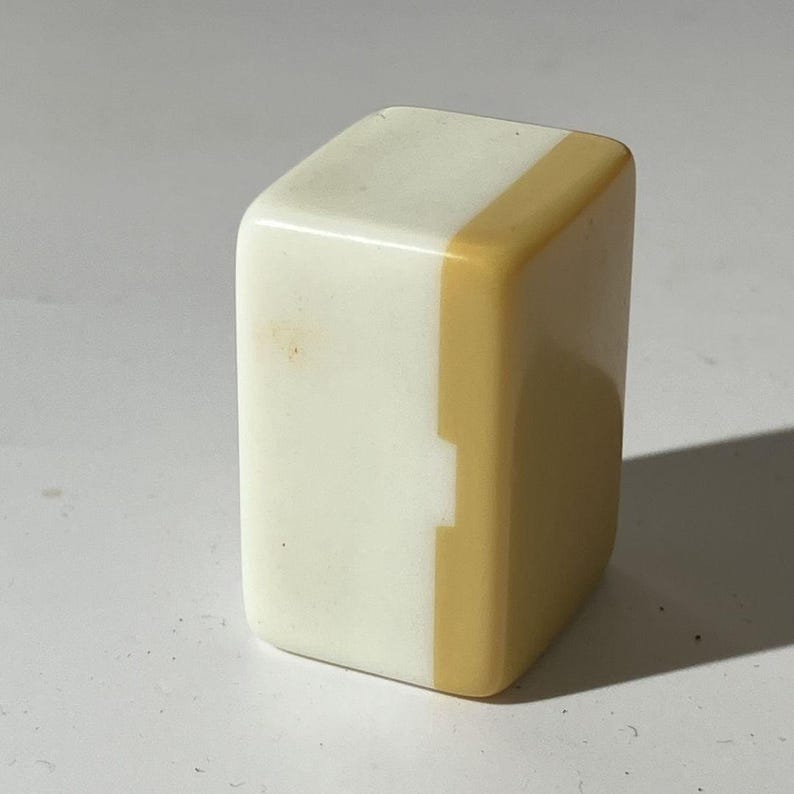 May include: A rectangular mahjong tile featuring a smooth, two-toned design. The left side is a solid, opaque off-white color, while the right side is a solid, opaque mustard yellow color. The tile has rounded edges and a glossy, polished finish.