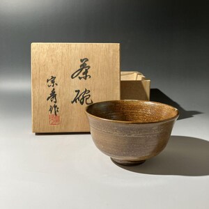 以下が含まれることがあります： 茶色の陶器のボウルで、広い縁と質感のある表面があります。 ボウルの隣には、日本語の文字と赤いスタンプが付いた木箱があります。 ボウルの直径は約15cmです。