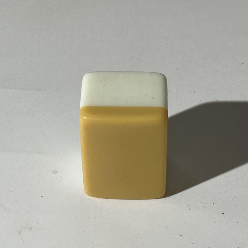 May include: A rectangular block with rounded corners, featuring a two-tone design. The top section is a solid opaque white, while the larger bottom section is a solid opaque mustard yellow. The object has a smooth, glossy finish throughout.