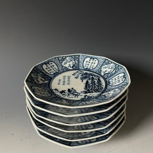 Könnte beinhalten: Ein Stapel von sechs blauen und weißen Porzellanplatten mit achteckiger Form. Die Platten zeigen ein Design aus Bäumen, Bergen und Figuren in Blau auf weißem Hintergrund. Das Design enthält chinesische Schriftzeichen.
