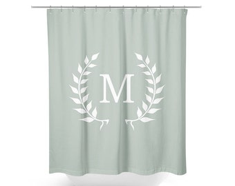 May include: A light green shower curtain with a white wreath and the letter "M" in the center.