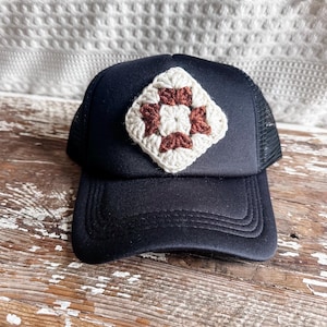 May include: A black trucker hat with a brown and white crocheted square patch on the front.